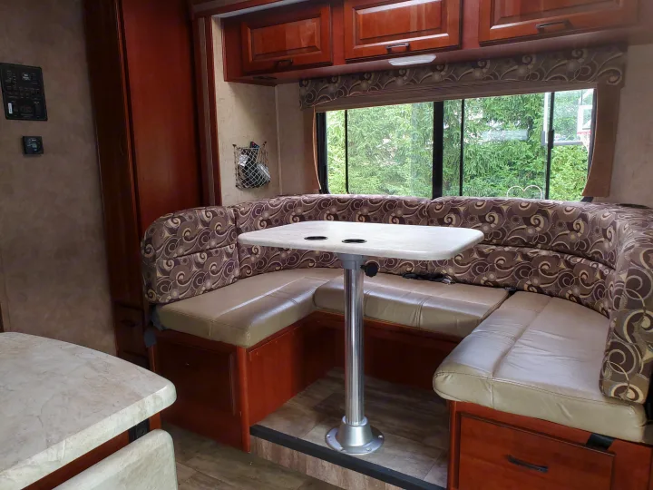 Spacious RV rental dinette featuring a U-shaped bench with patterned cushions, table, and large windows.. Forest River Sunseeker 2016