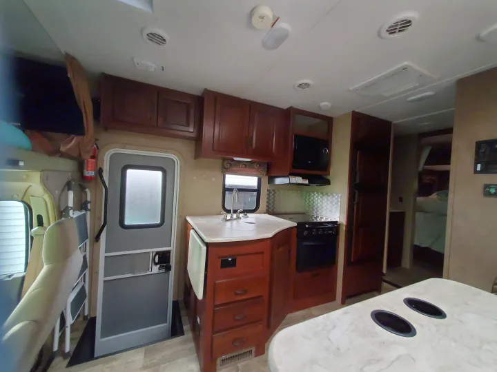 Inside an RV rental: full kitchen with microwave, sink, stove, plus living area and a glimpse of the sleeping quarters.. Forest River Sunseeker 2016