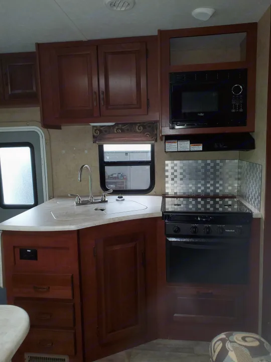 RV rental kitchen: modern dark wood cabinets, light counter, sink, stove, microwave, & metal backsplash.. Forest River Sunseeker 2016