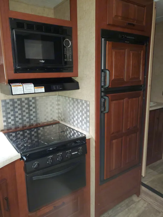 Compact RV rental kitchen with High Pointe microwave, Suburban range, Dometic refrigerator, and metallic tiled backsplash.. Forest River Sunseeker 2016