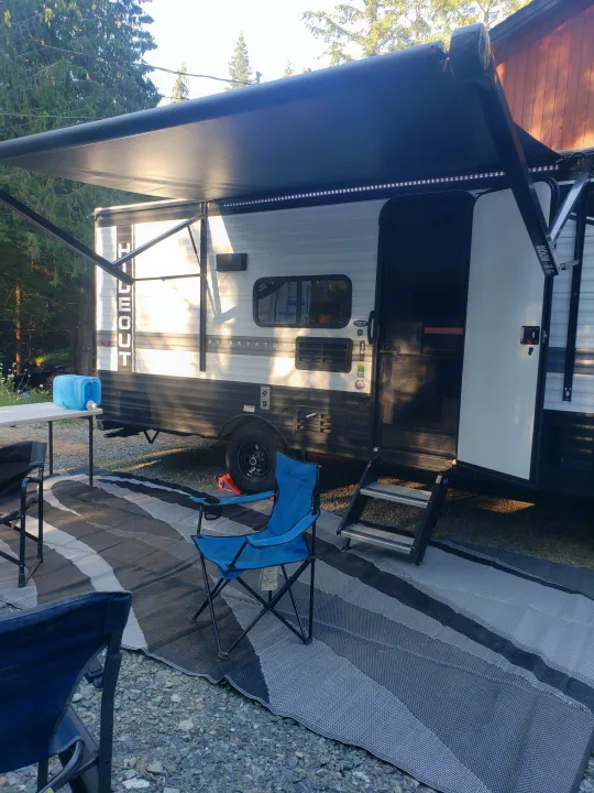 An RV rental at a scenic campsite with its awning extended, featuring LED lights, chairs, and an outdoor mat.. Keystone RV Hideout 2022