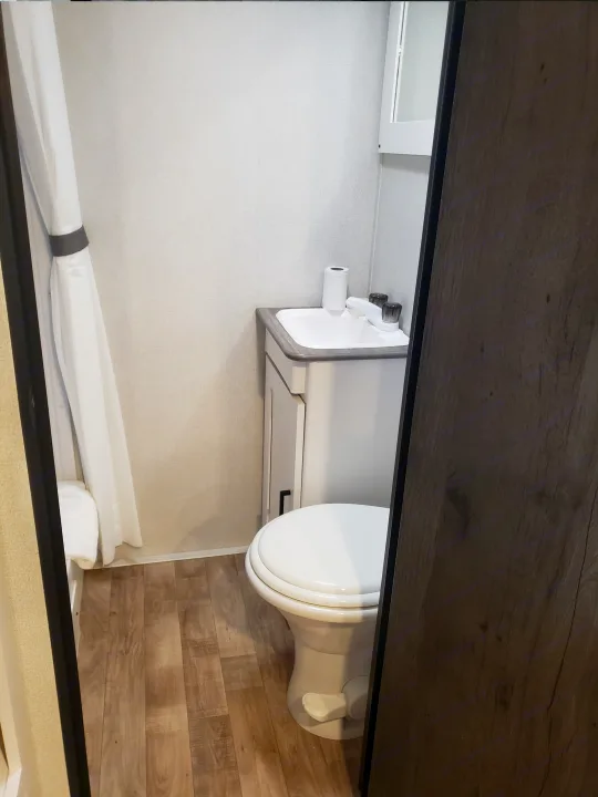 A compact and bright RV rental bathroom features a white toilet, small sink, and shower area with a white curtain.. Keystone RV Hideout 2022