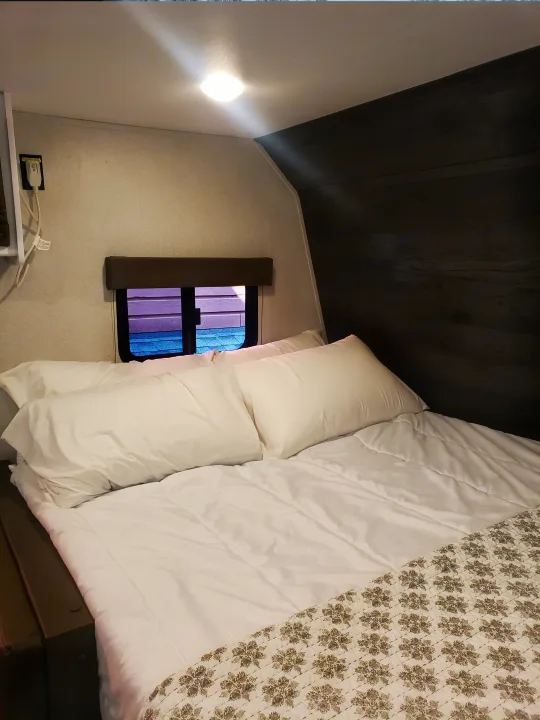 Cozy RV rental bedroom with a neatly made bed, white linens, patterned blanket, and a small window for natural light.. Keystone RV Hideout 2022