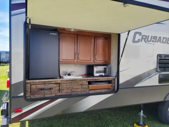 An rv rental showcases its exterior kitchen, complete with a fridge, sink, overhead cabinets, and a toaster oven, ideal for outdoor cooking.. Crusader Crusader Fifth Wheel 2016