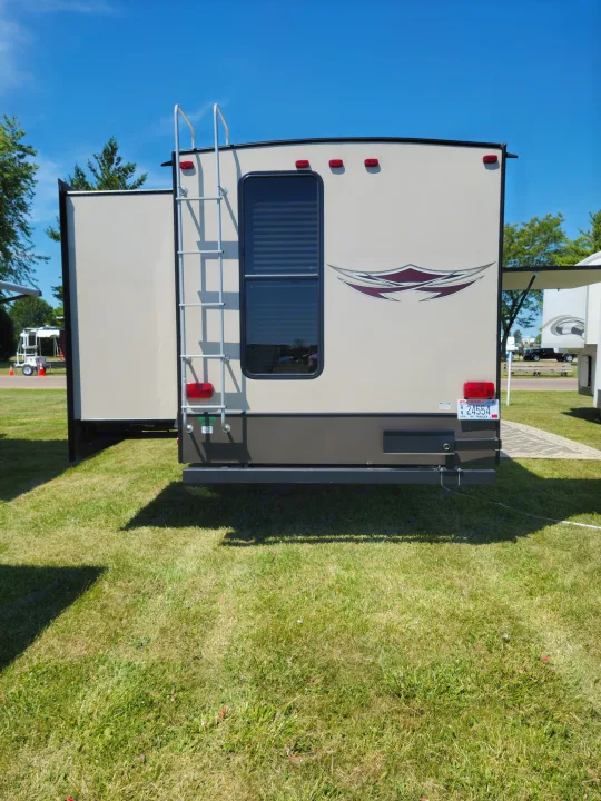 Rear exterior of an RV rental: ladder, window, and extended slide-out. Wisconsin plate visible on sunny grass.. Crusader Crusader Fifth Wheel 2016