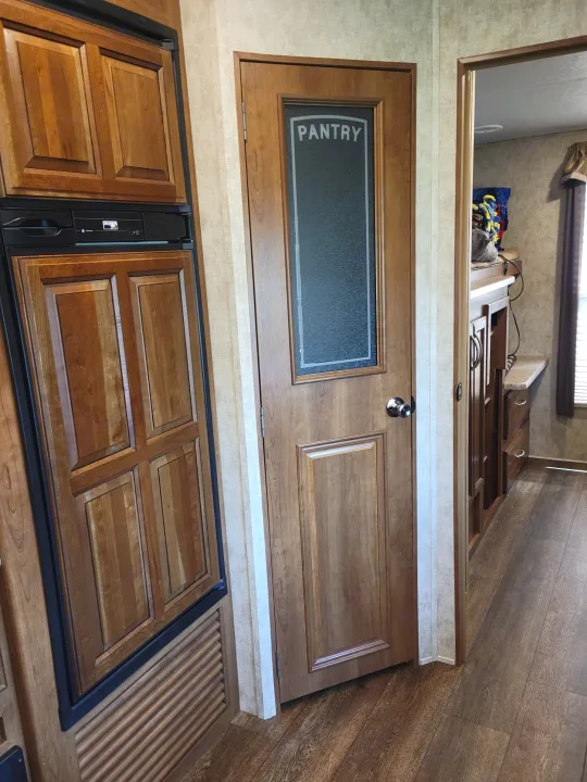 RV rental interior featuring a wood-paneled refrigerator, a pantry door with frosted glass, and a view into the mobile living area.. Crusader Crusader Fifth Wheel 2016