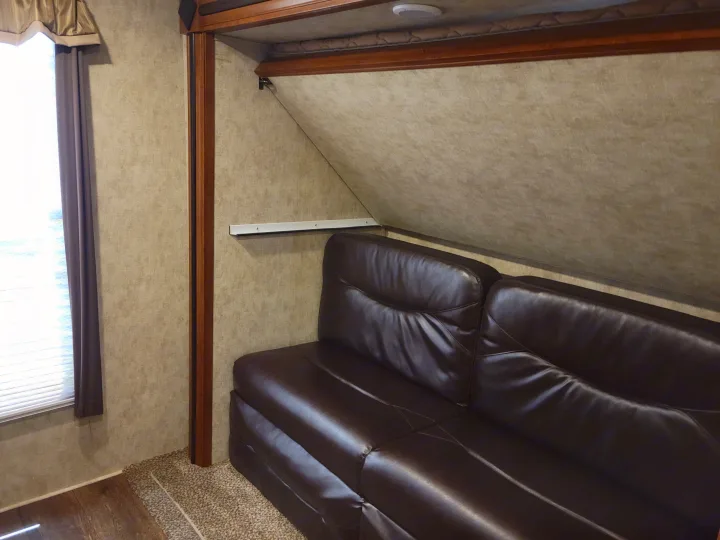 Inside this RV rental: a dark leather sofa below a stowed bunk bed, with a window offering natural light.. Crusader Crusader Fifth Wheel 2016