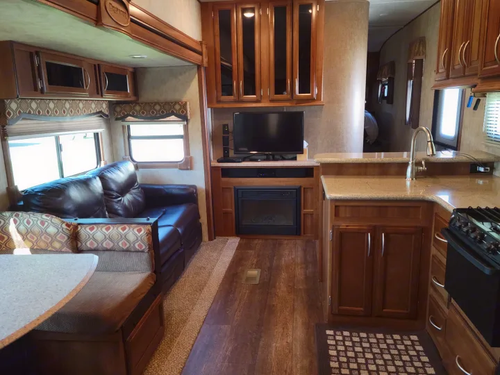 Spacious RV rental interior featuring a modern kitchen with sink & stove, comfy living room with sofa, TV, fireplace, and dining booth.. Crusader Crusader Fifth Wheel 2016