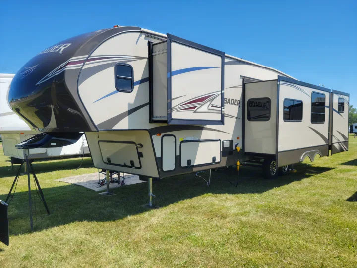 This large beige and black fifth-wheel RV, a potential rv rental, is set up on grass with extended slide-outs under a clear sky.. Crusader Crusader Fifth Wheel 2016