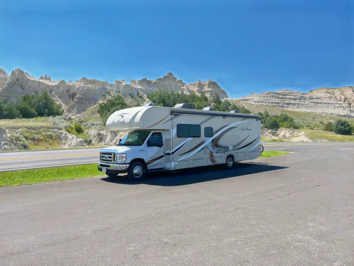 Four Winds RV rental parked by stunning badlands formations under a clear blue sky, ideal for scenic adventures.. Thor Motor Coach Four Winds 2018