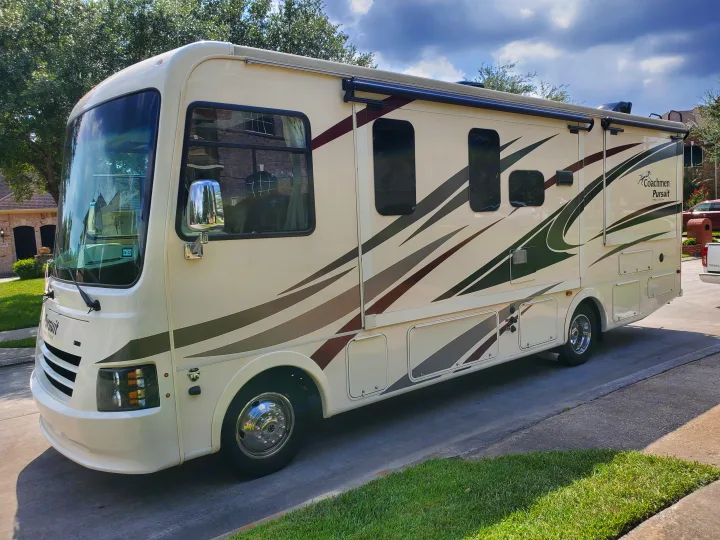 Cream Coachmen Pursuit RV rental with green/burgundy graphics, parked on a paved driveway. Ideal for travels.. Coachmen Pursuit 27DS 2018