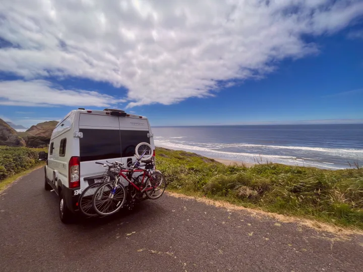 White RV rental with bikes parked on a scenic coastal road, overlooking the ocean and sandy beach.. Winnebago Winnebago 2023