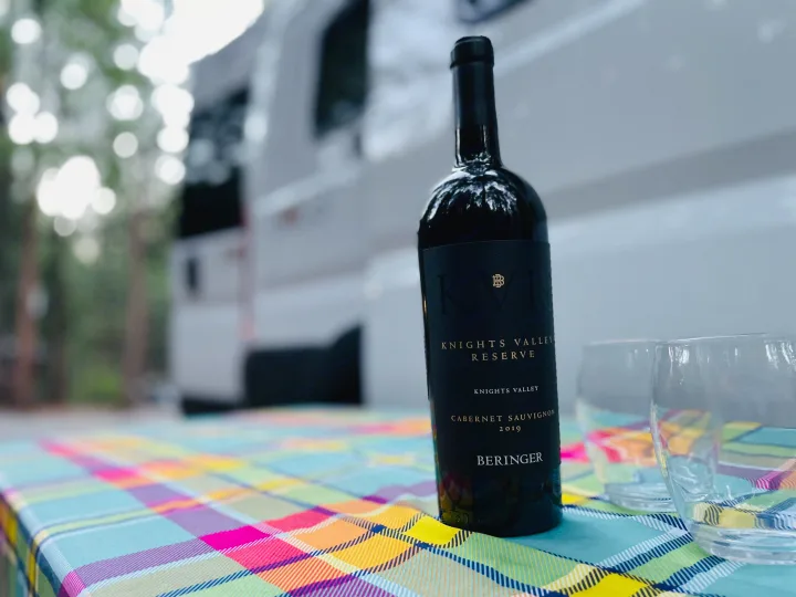 A bottle of Beringer Cabernet Sauvignon and two glasses on a plaid table, with an rv rental blurring in the background. Perfect outdoor setting.. Winnebago Winnebago 2023