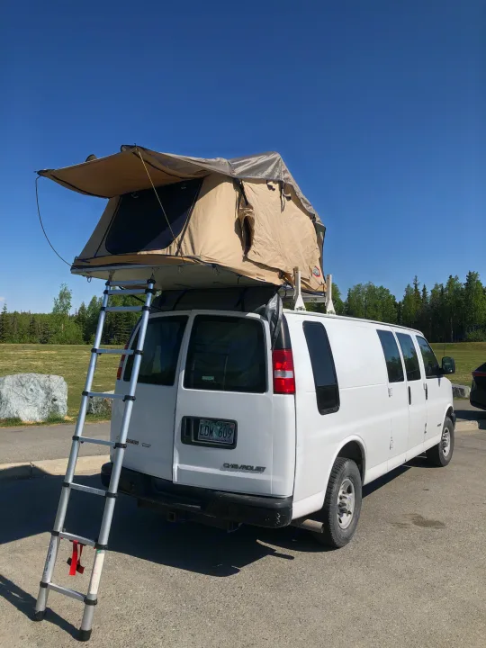 White Chevy van with rooftop tent and ladder, an ideal RV rental for camping adventures.. Chevrolet Other 2006