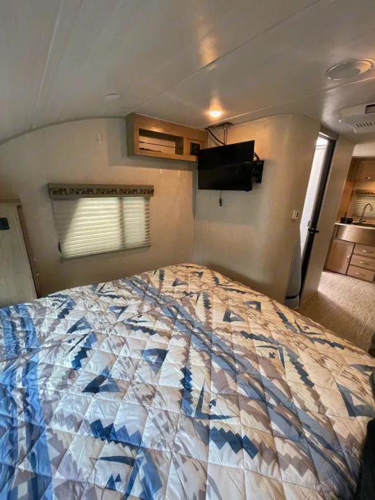 This comfortable RV rental bedroom features a patterned bed, wall-mounted TV, and window, perfect for your travel adventures.. R-Pod Hood River Edition 2020