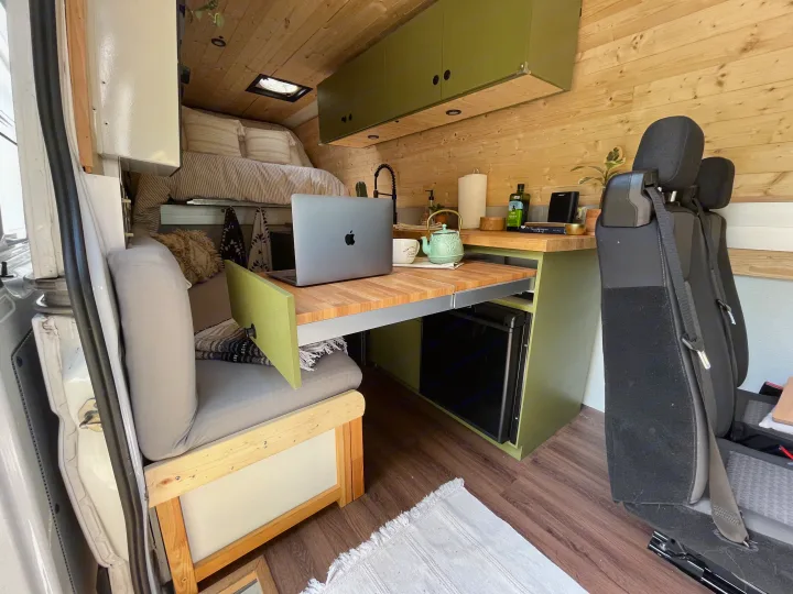Inside a modern RV rental: wood-paneled camper van with a cozy bed, compact kitchen, and a pull-out laptop workspace.. Freightliner Sprinter 2010