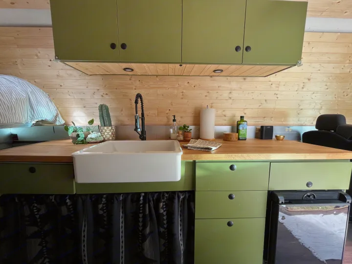 Compact RV rental kitchen with olive green cabinets, wooden walls, a white sink, and wood countertop.. Freightliner Sprinter 2010