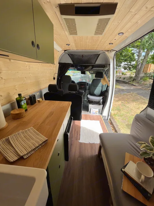 Inside a modern RV rental, showcasing a functional kitchen, cozy bed, and bright wooden interior.. Freightliner Sprinter 2010