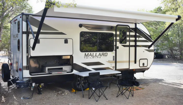 This Mallard Tailwind RV rental is set up at a campsite with an extended awning and outdoor kitchen.. Heartland RVs Mallard 2022