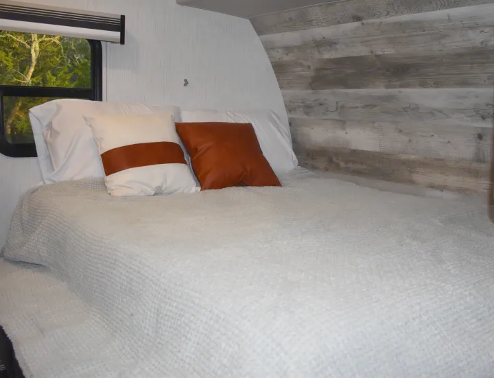 Comfortable RV rental bedroom with bed, white sheets, stylish pillows, textured blanket, and a wood plank accent wall.. Heartland RVs Mallard 2022