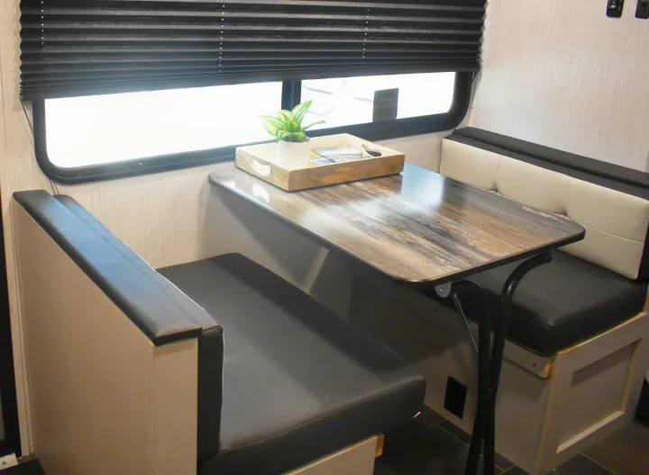 Cozy RV rental dinette with bench seats, a wood-look table, and window with black pleated blinds.. Heartland RVs Mallard 2022