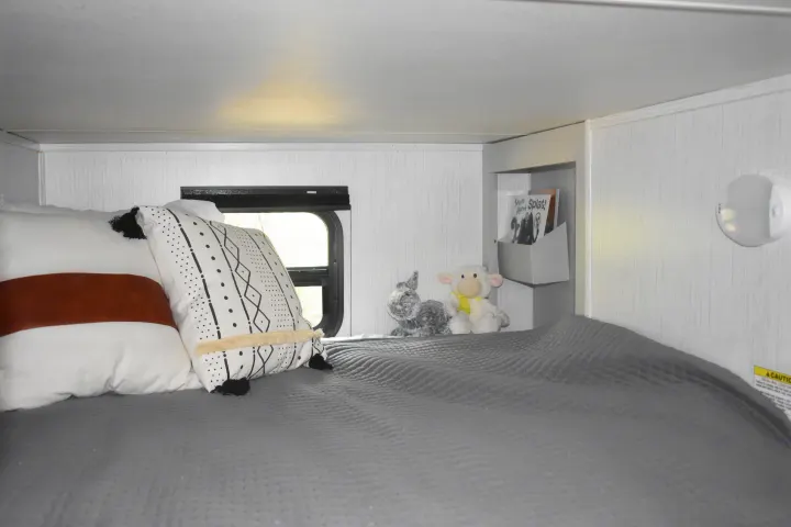 Cozy RV rental bunk bed with plush pillows, a window, stuffed animals, and storage for books, creating a comfortable travel space.. Heartland RVs Mallard 2022