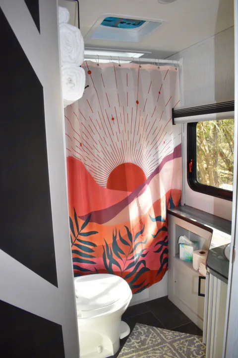 Bright RV rental bathroom: unique sunset shower curtain, toilet, and convenient storage.. Heartland RVs Mallard 2022