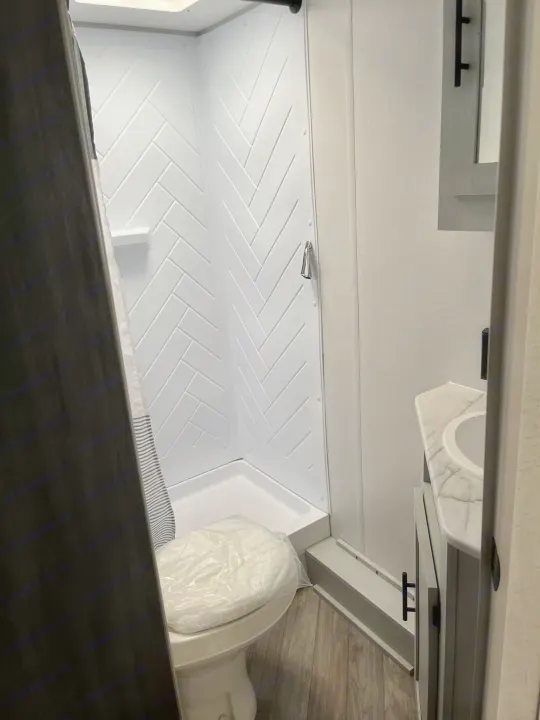 RV rental bathroom featuring a corner shower with herringbone walls, a toilet with a plastic cover, and a vanity.. Forest River Wildwood FSX 2022