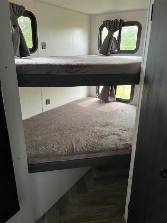 Cozy RV rental interior: stacked bunk beds with plush grey bedding and windows with curtains, ideal for sleeping.. Forest River Wildwood FSX 2022