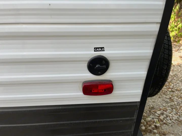 RV rental's white corrugated side, showing the cable input and red reflector light for your travel setup.. Forest River Wildwood FSX 2022