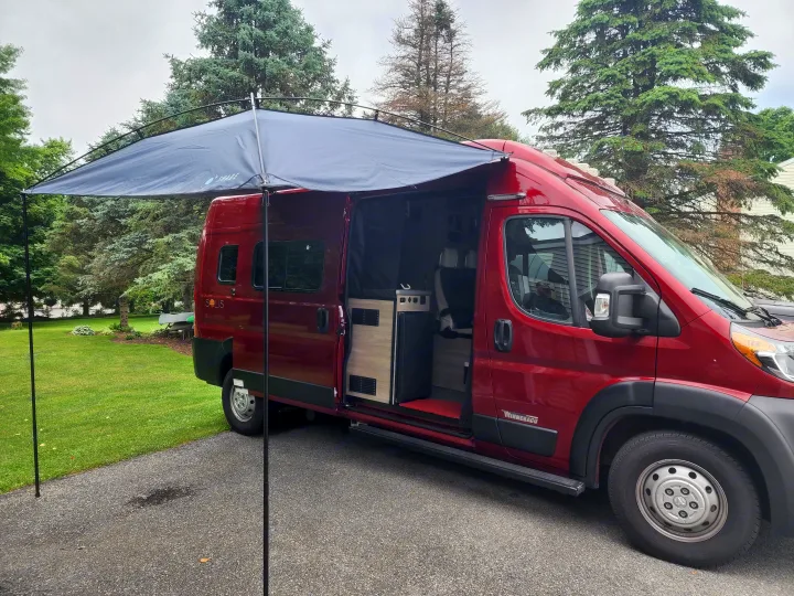 A red Winnebago Solis camper van with extended awning & open side door, showcasing interior. Ideal for rv rental.. Winnebago Solis 2022