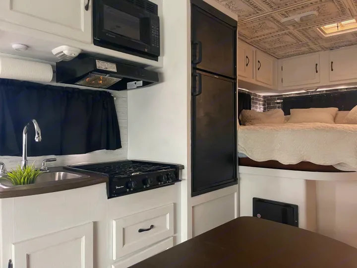 Clean, modern RV rental interior featuring a full kitchen (sink, stove, microwave, fridge) and comfortable bed with white bedding.. Forest River Coachmen Freelander 2010