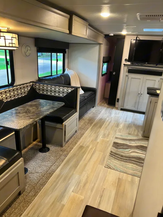 Inside a stylish rv rental: spacious living area with booth seating, sofa, TV, and light wood flooring.. PrimeTime 31BHD 2021