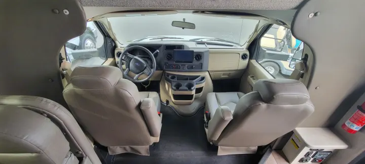 Inside an RV rental: front cabin with beige swivel seats, functional dashboard, and various controls.. Jayco Greyhawk 2021