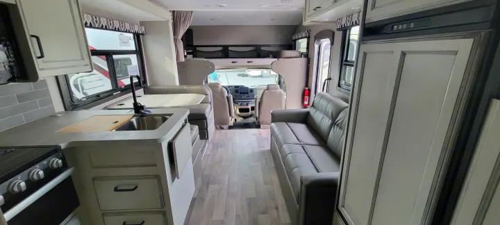 Interior view of a modern rv rental, showcasing kitchen with sink, dinette, sofa, and driver's area up front.. Jayco Greyhawk 2021