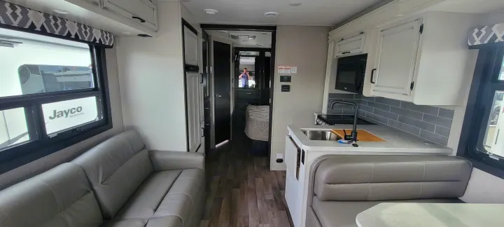 Modern RV rental interior: living area with sofa, kitchen with sink, dinette, and a bedroom visible beyond.. Jayco Greyhawk 2021