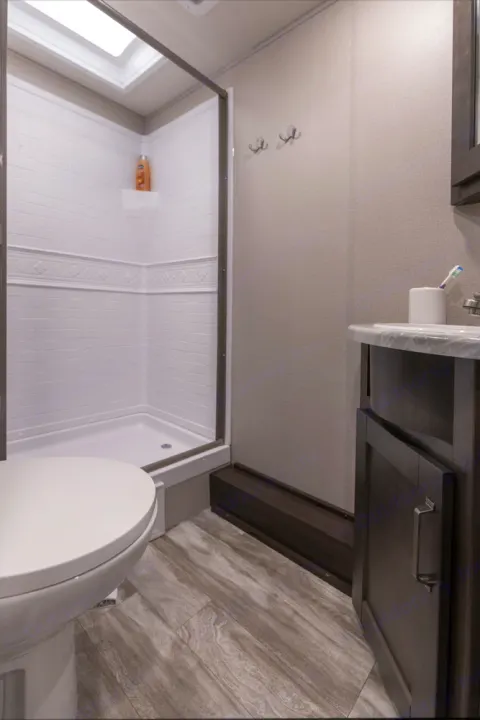 Modern RV rental bathroom with a stand-up shower, toilet, and vanity sink. Includes hooks for towels or clothes.. Grand Design Transcend Xplor 2022