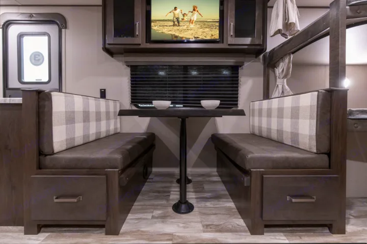 RV rental dinette with two benches featuring plaid backrests, a table, a TV, and adjacent bunk beds.. Grand Design Transcend Xplor 2022