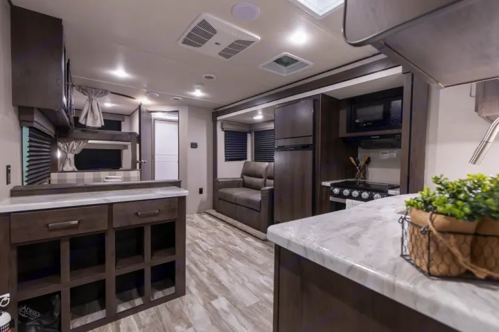 Bright rv rental interior showcasing a modern kitchen, bunk beds with privacy curtains, and a comfy sofa with wood-look flooring.. Grand Design Transcend Xplor 2022