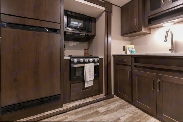 Modern RV rental kitchen features dark wood fridge, microwave, stove/oven, sink, and storage cabinets.. Grand Design Transcend Xplor 2022