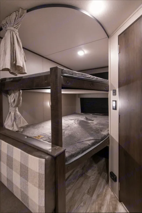 Cozy bunk beds in an RV rental, featuring dark wood frames, grey bedding, and privacy curtains. Ideal for family travel.. Grand Design Transcend Xplor 2022