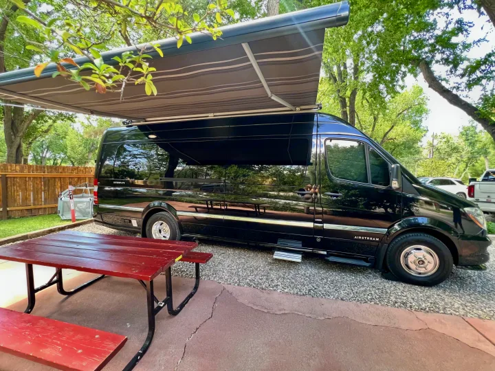 An Airstream Interstate rv rental with its awning extended, parked on gravel next to a red picnic table at a campsite.. Airstream Interstate 2016