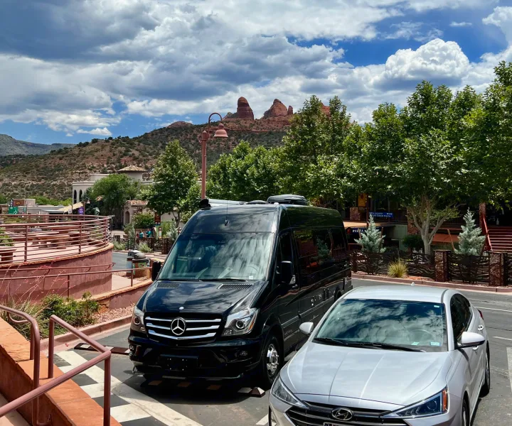 Black luxury van (potential RV rental) and silver car parked in scenic Sedona, Arizona, amidst red rock mountains & greenery.. Airstream Interstate 2016