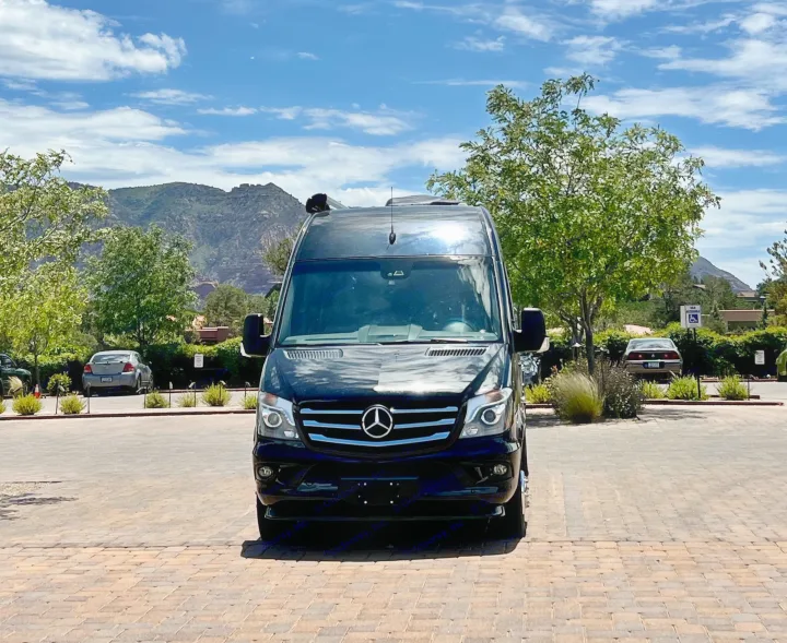 Black Mercedes Sprinter van, ready for an RV rental adventure, parked on a paved lot with mountains under a blue sky.. Airstream Interstate 2016