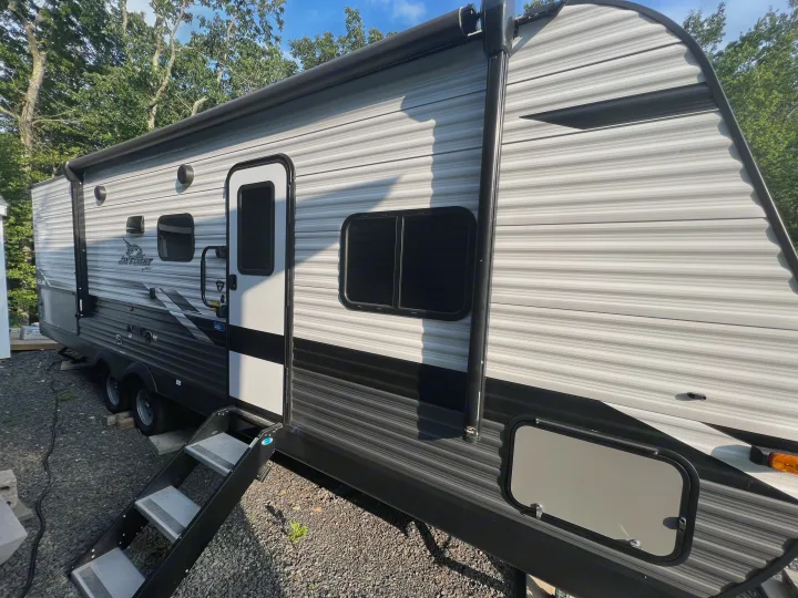 Grey and black rv rental travel trailer parked outdoors, showing the side, steps, main door, and windows.. Jayco Jay Flight SLX 2022