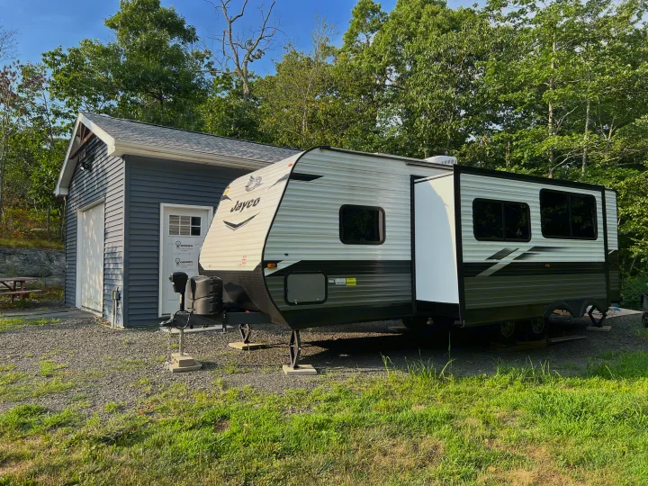 Experience nature: a modern Jayco RV rental with extended slide-out, parked on gravel next to a grey building.. Jayco Jay Flight SLX 2022