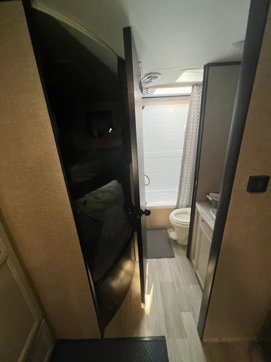 This RV rental interior showcases a compact bathroom with a shower/tub, toilet, and vanity. Bunk beds are visible on the left.. Jayco Jay Flight SLX 2022