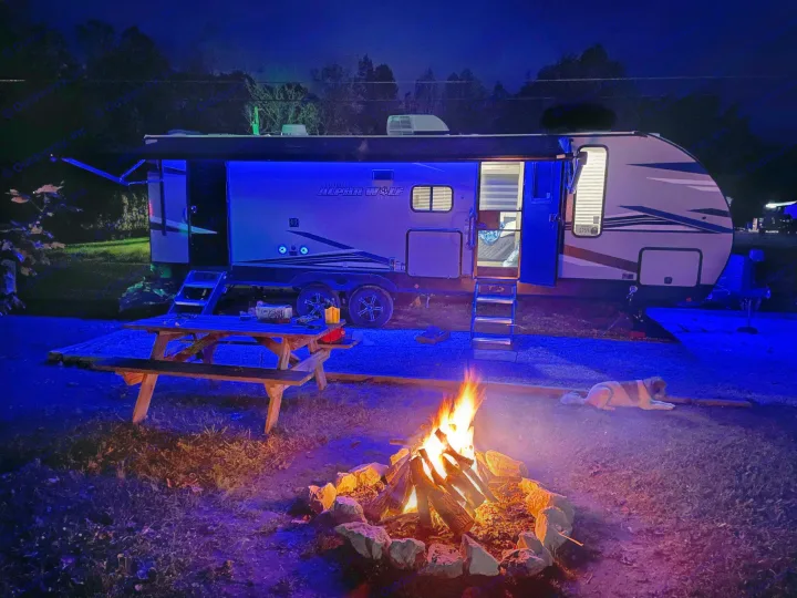 Enjoying a peaceful night by the campfire with our RV rental and furry friend. Blue lights illuminate the scene.. Forest River Cherokee Alpha Wolf 2022