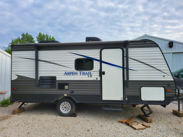 An Aspen Trail LE travel trailer, ideal for RV rental, parked on gravel. Stabilizing jacks are visible, ready for outdoor trips.. Aspen Trail LE 2020