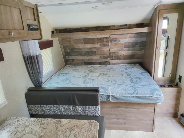 RV rental interior with a cozy bed, wood accent wall, built-in dinette, and storage for comfortable travel.. Aspen Trail LE 2020